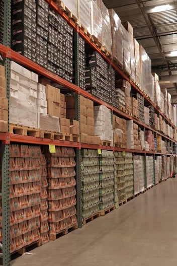Wholesale food warehouse aisle with pallets of boxed and shrink-wrapped products on tall orange racking